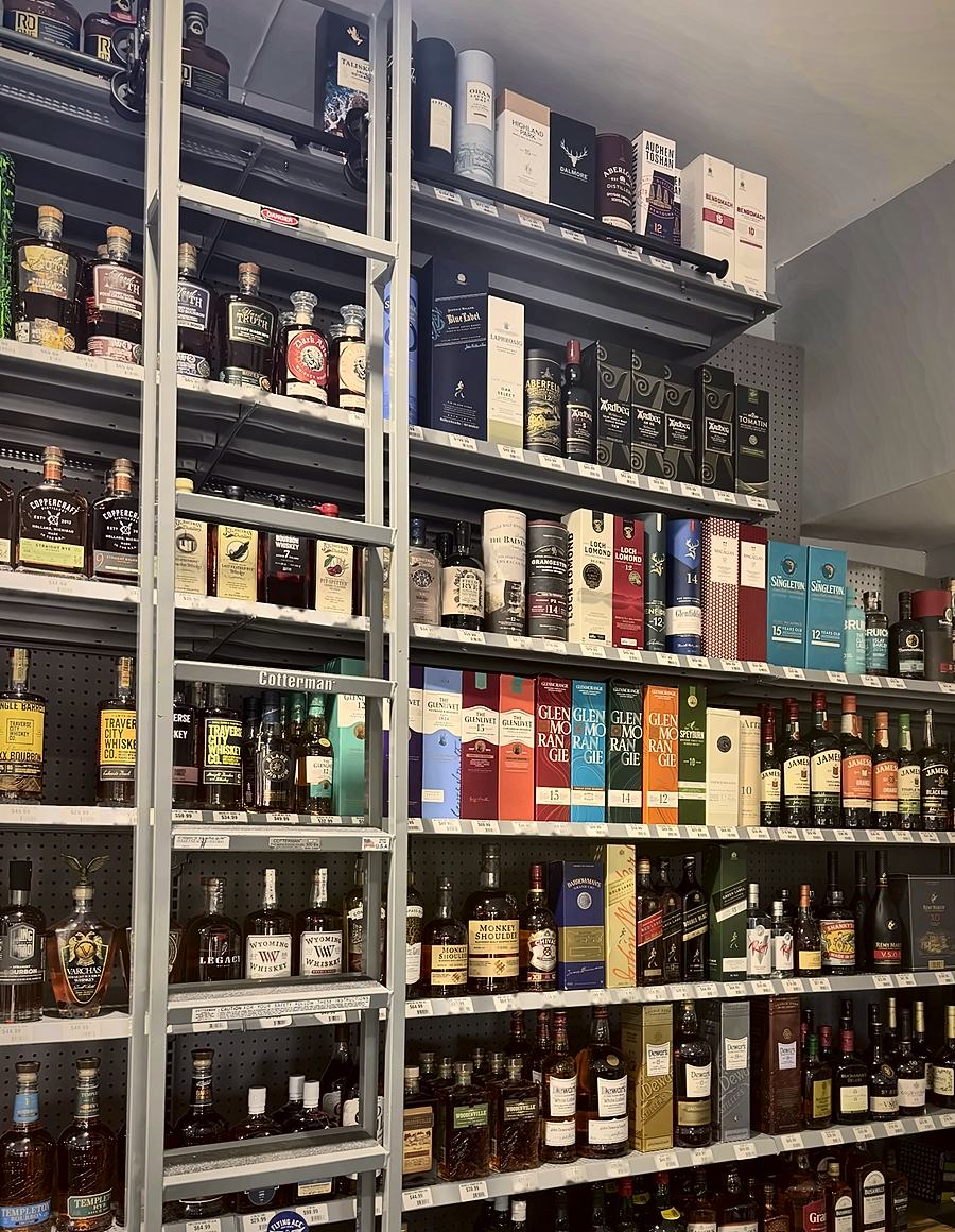 Top shelves of boxed single malt Scotch, including Johnnie Walker Blue Label, Ardbeg and Laphroaig, beside a rolling library ladder